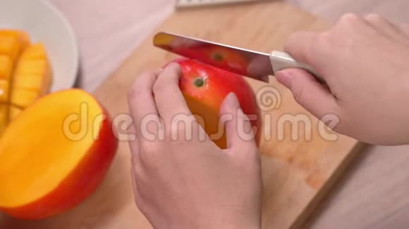年轻女子正在切一个漂亮的新鲜多汁的芒果放在木桌上吃厨房里的砧板上4K视频的预览图