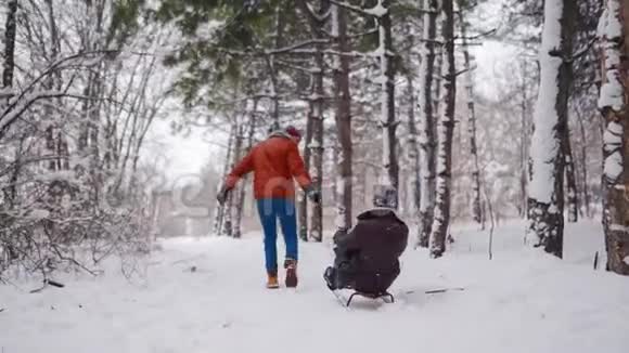 可爱的夫妇在下雪的冬天滑雪下雪时男人和女朋友拉雪橇女人玩得开心视频的预览图