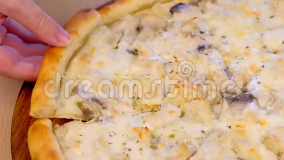 男人在桌子上的木板上拿一片比萨饼上面有蘑菇香瓜和奶酪特写的手视频的预览图