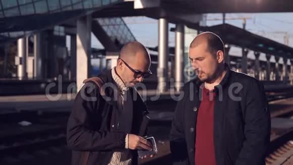 两名男子在火车站月台上等着火车的到来聊着天为这次旅行兴奋不已视频的预览图