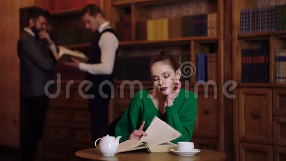 图书馆概念女孩翻书在图书馆喝茶在后台两个男人说话视频的预览图