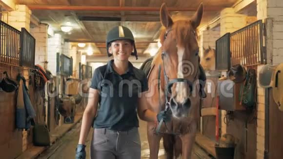 年轻的女骑师带着一匹棕马穿过马厩视频的预览图