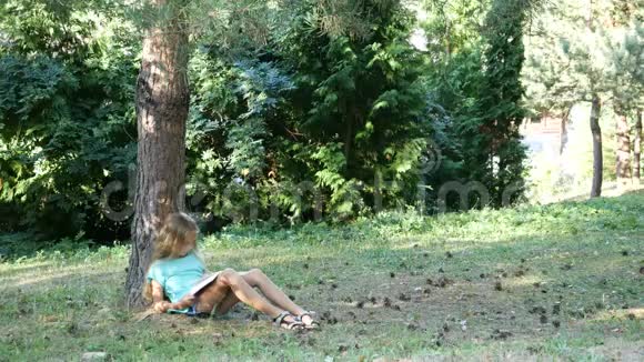 一个十几岁的女孩在树下看书公园里的夏日阅读视频的预览图