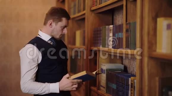 一个穿西装的人在图书馆的书架旁看一本大书学习观念视频的预览图