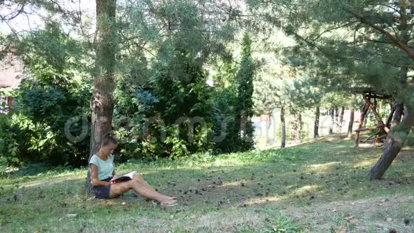 在树林里休息的地方女孩在树下的草坪上看书视频的预览图