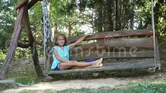 迷人的赤脚女孩对着镜头微笑在公园的一个大秋千上休息愉快视频的预览图