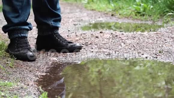 森林小径上的水坑里的人库存录像站在水坑边思考如何走的人的脚视频的预览图