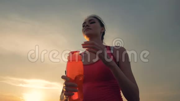苗条漂亮的女人正在新鲜的空气中奔跑从瓶子里喝东西视频的预览图