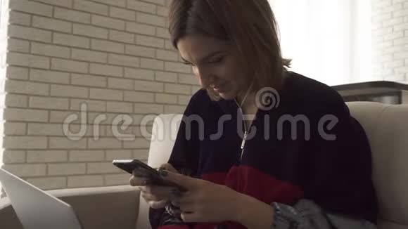 一个女孩在手机上打字然后微笑着在笔记本电脑上打字键盘上的女性打字工作的自由职业者女孩视频的预览图