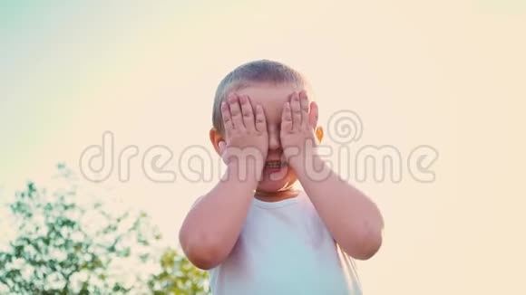 四岁的男孩穿着一件白色t恤笑着用手捂住脸一个活泼开朗的孩子在视频的预览图