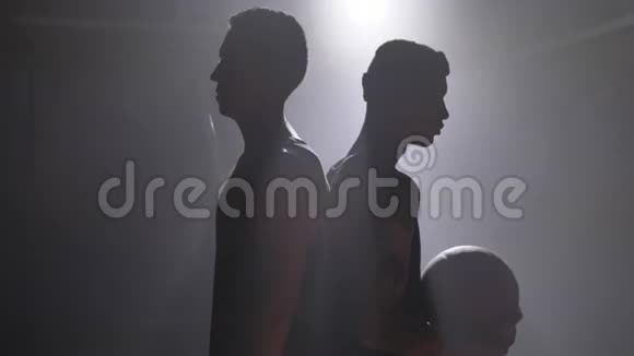 两名篮球运动员的身影背靠背站在房间里烟雾和泛光灯视频的预览图