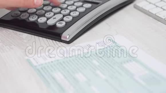 电脑键盘和电脑旁边桌子上的妇女填写1040税单和计算退税的特写镜头视频的预览图