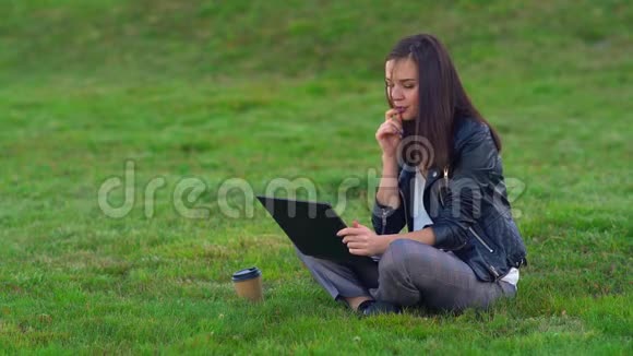 一个年轻迷人的女孩在公园的草坪上做梦在笔记本电脑上写了一个关于自己的故事视频的预览图