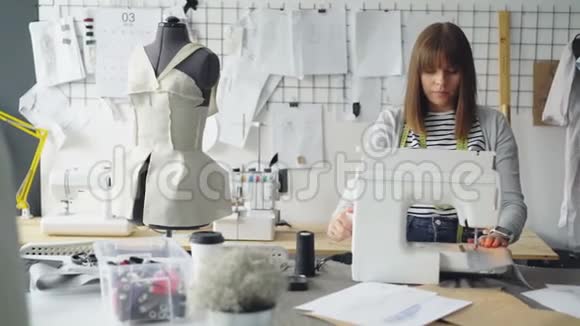 自谋职业的服装设计师正在使用缝纫机缝制纺织品并查看躺在上面的草图视频的预览图
