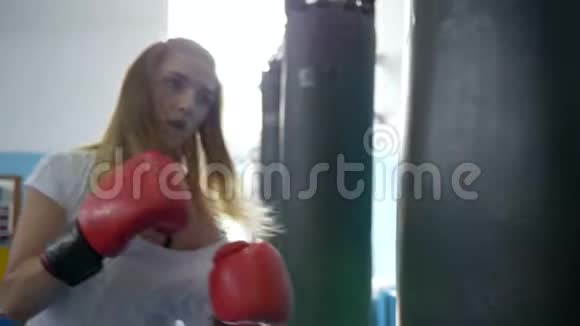体育俱乐部拳击手训练运动女孩戴红手套打拳打袋视频的预览图