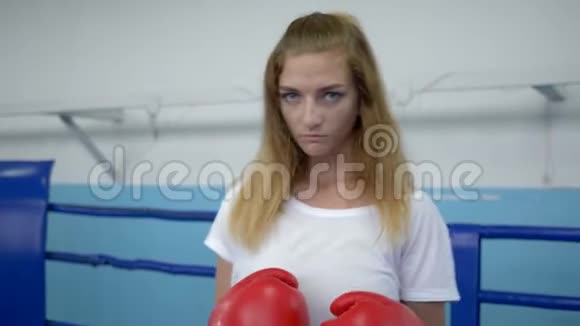 拳击场上的运动女孩在拳击手套上准确地打拳在锻炼时看着摄像机视频的预览图