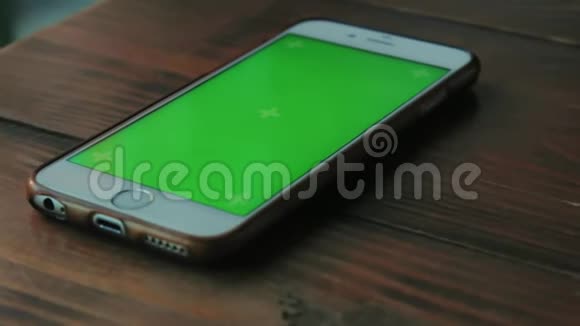 一个绿色屏幕的白色手机在咖啡馆的深棕色木桌上视频的预览图