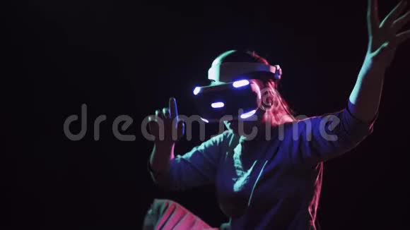 穿着VR耳机在黑暗背景下做手势的年轻女子视频的预览图