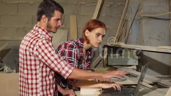 两个木匠在他们的车间里用笔记本电脑做家具视频的预览图
