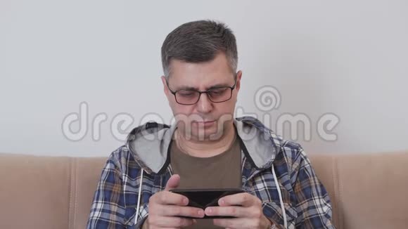 一位戴眼镜的中年男子正在智能手机上使用移动互联网而坐在房间的沙发上视频的预览图