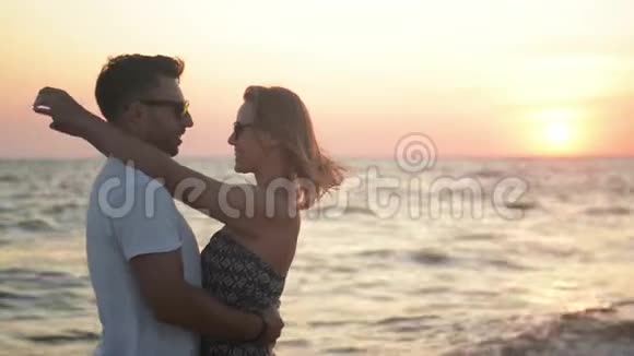 一对夫妇在日落时在海滩上拥抱和亲吻眺望大海视频的预览图