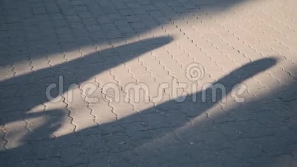 一对相爱的年轻夫妇在人行道上的黄昏阴影太阳下两个人的剪影男女步行视频的预览图