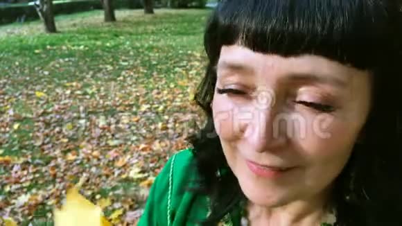 美丽幸福的女人穿着绿色的裙子在秋天的公园里分拣和玩黄色的叶子视频的预览图