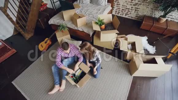 幸福的年轻夫妇在搬到新公寓后打开盒子拿东西和聊天这是他们的最大景观视频的预览图