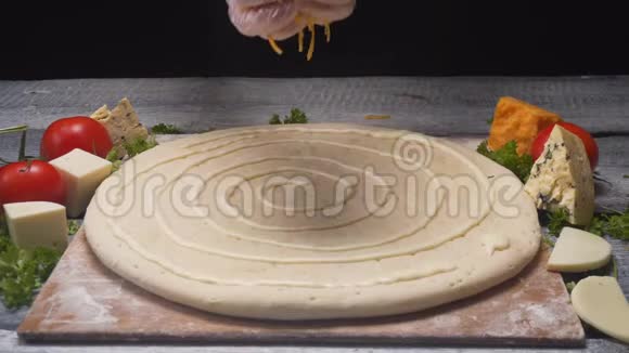 厨师在其他配料前用切达干酪在木板上覆盖比萨饼面团框架视频的预览图