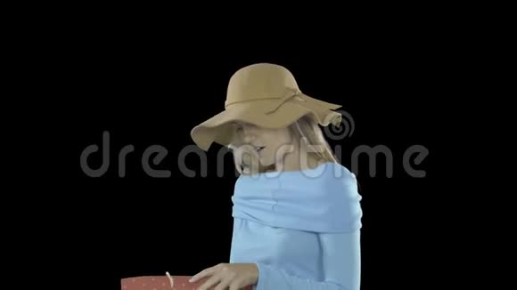 优雅的年轻女士留着长发脸上长着雀斑戴着肉色的帽子看着包微笑着视频的预览图