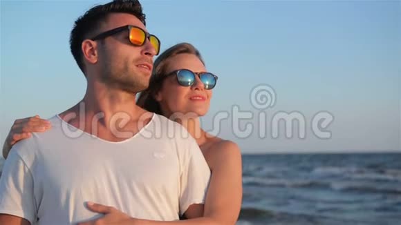 在阳光明媚的夏日幸福的微笑夫妇戴着时尚的太阳镜拥抱在海边的海滩上视频的预览图