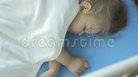 两岁的小女孩睡在铺着白色毯子的婴儿床上日间睡眠视频的预览图