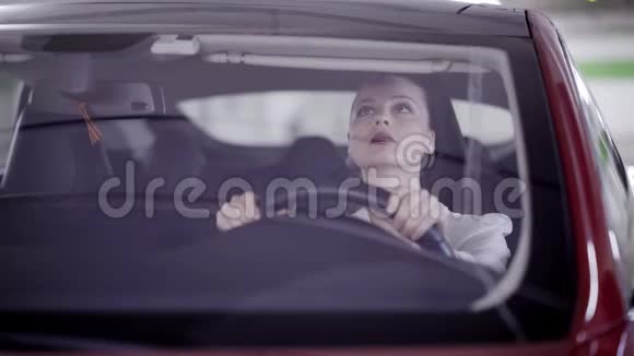 穿着白色衬衫的漂亮女人坐在方向盘后面的红色汽车上视频的预览图
