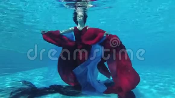 快乐的女孩新娘穿着红色的连衣裙手里拿着红色和蓝色的布潜入水中到游泳池的底部视频的预览图