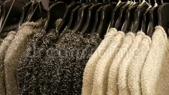 一排漂亮的暖女人一件毛茸茸的黑白相间的毛衣挂在商店的黑色衣架上视频的预览图