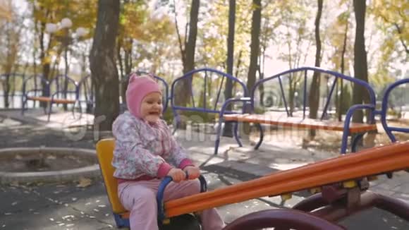 秋天城市公园秋千上戴着粉红色帽子的小女孩视频的预览图