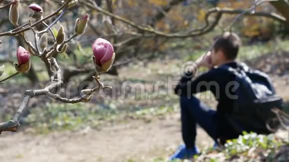 年轻悲伤的家伙背着背包坐在公园里背景是木兰花视频的预览图