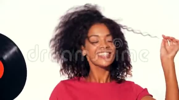 年轻漂亮的非洲裔美国妇女穿着红色上衣在白色背景下与乙烯基唱片一起享受和跳舞现代视频的预览图