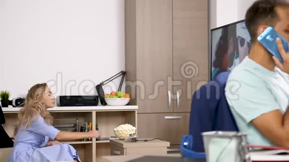 女人一边吃爆米花一边看电视一边丈夫在用手机说话视频的预览图