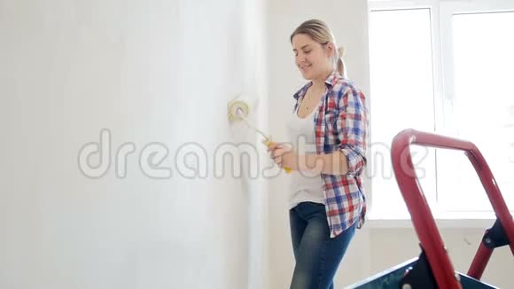 一个美丽的年轻女子穿着格子衬衫在她的房子里做装修年轻女孩用油漆粉刷墙壁视频的预览图
