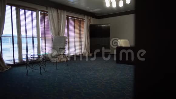 大房间有大窗户桌子扶手椅和蓝色地毯现代酒店客房视频的预览图