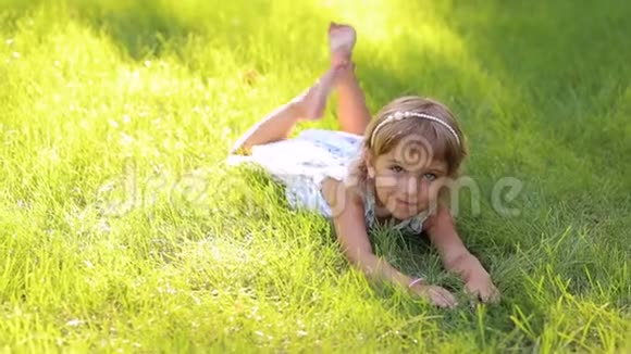天气炎热的阳光公园里穿着裙子躺在绿草上的小可爱女孩视频的预览图