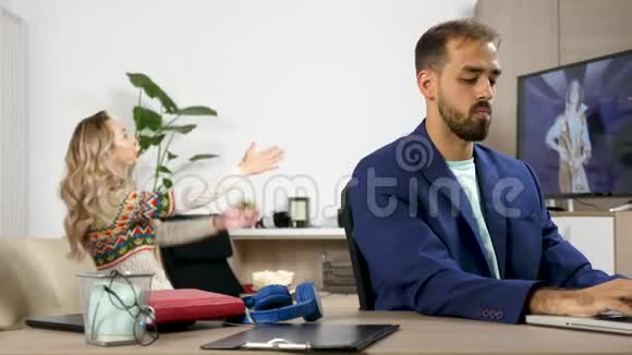 女人一边看电视一边在后台吵闹一边丈夫尝试用笔记本电脑工作视频的预览图