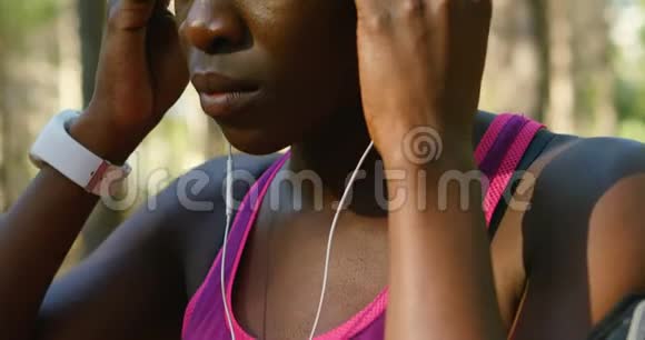 女运动员在森林里举着耳机视频的预览图