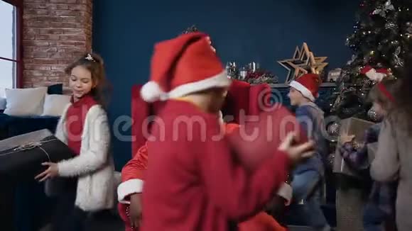 穿着红色圣诞老人服装的快乐的非洲男人坐在椅子上微笑的孩子们围着他跳来跳去视频的预览图