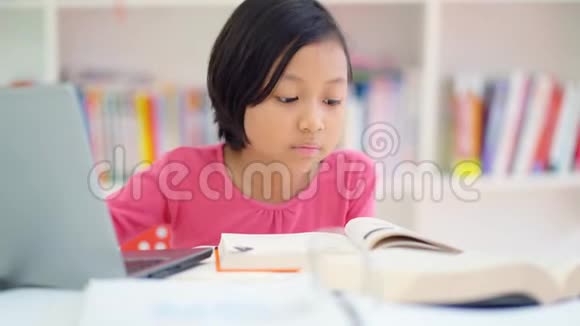 小女孩一边看书一边用笔记本电脑视频的预览图