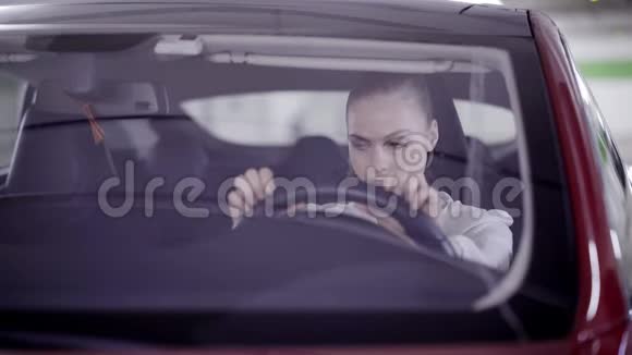 马尾辫可爱的女孩坐在红色的车里摇着头在方向盘后面视频的预览图