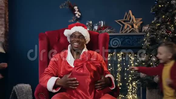 圣诞老人戴着帽子坐在红色的椅子上五个孩子意外地跑着拥抱他视频的预览图