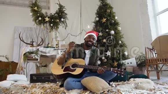 快乐的非洲男人带着吉他和孟加拉灯坐在地板上背景是闪闪发光的金色纸屑视频的预览图