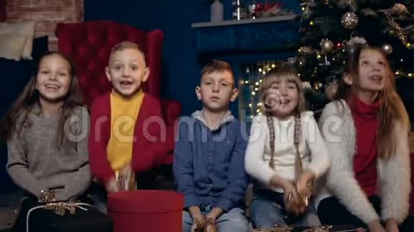 快乐的孩子们拿着礼物坐在圣诞树旁开始扔五彩纸屑的画像视频的预览图